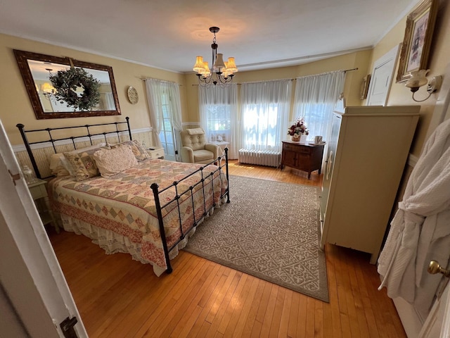 bedroom with an inviting chandelier, radiator heating unit, crown molding, and light hardwood / wood-style flooring