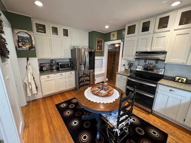 kitchen featuring appliances with stainless steel finishes, radiator, white cabinets, backsplash, and light hardwood / wood-style flooring