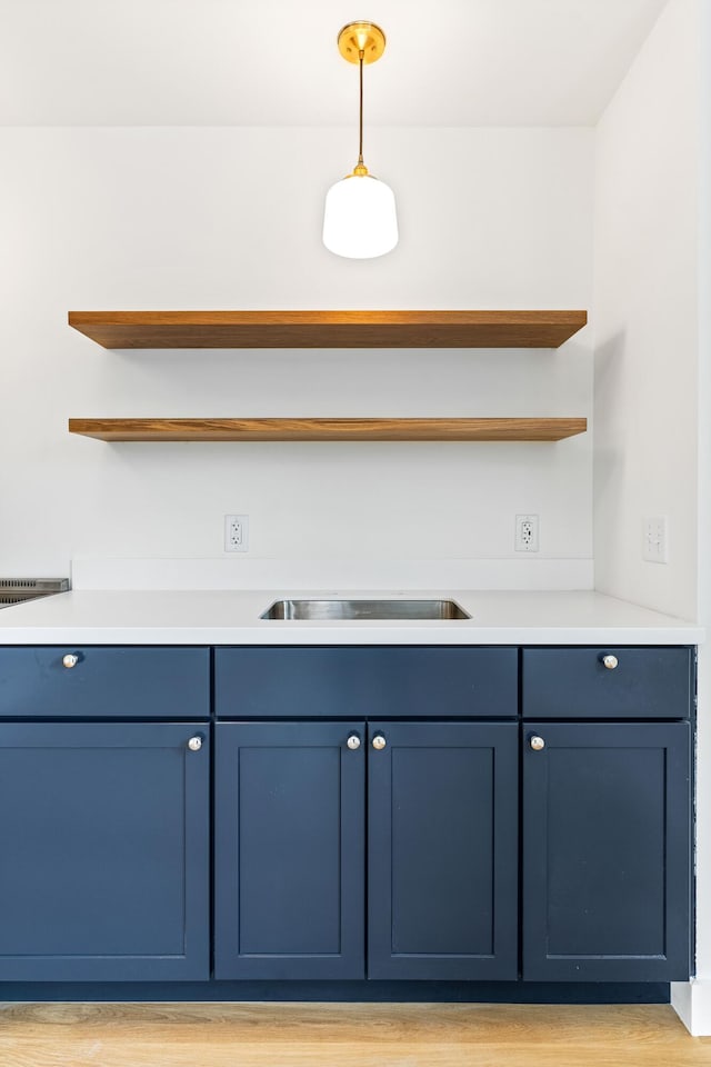 bar featuring blue cabinetry, cooktop, hanging light fixtures, and light hardwood / wood-style flooring