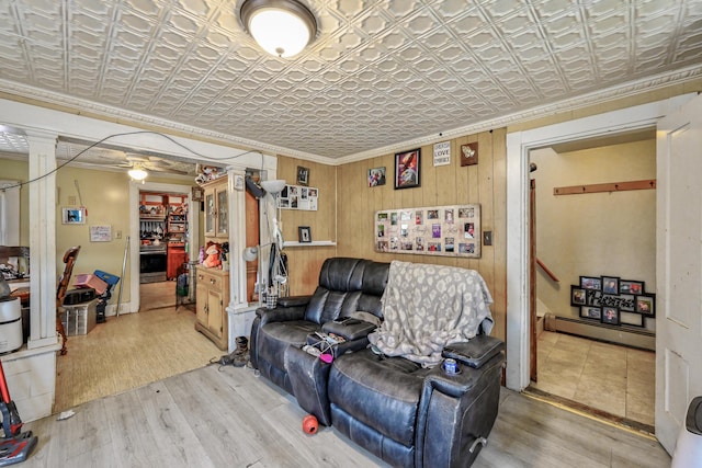 living room featuring baseboard heating, ceiling fan, crown molding, wood walls, and hardwood / wood-style floors