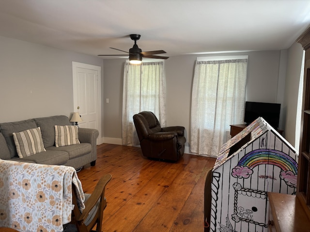 living area with baseboards, hardwood / wood-style flooring, and a ceiling fan