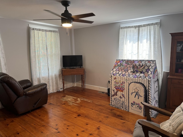 living area featuring baseboards, visible vents, a ceiling fan, and wood-type flooring