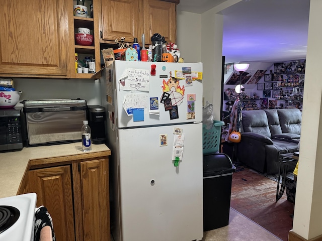 kitchen with light countertops, stainless steel microwave, range, freestanding refrigerator, and brown cabinets
