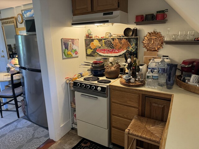 kitchen featuring tile counters, white electric range oven, ventilation hood, and freestanding refrigerator