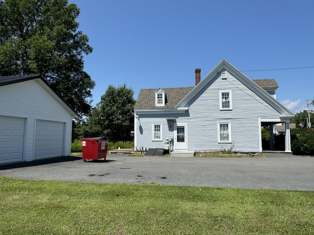 view of front of house with a front yard, a chimney, an outbuilding, a shingled roof, and a garage