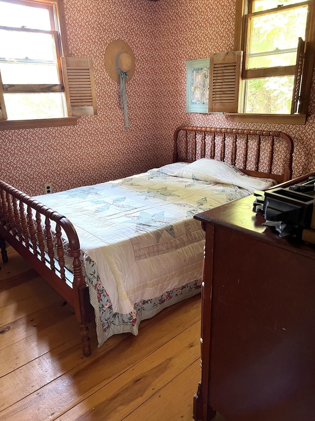 bedroom featuring multiple windows, wood-type flooring, and wallpapered walls