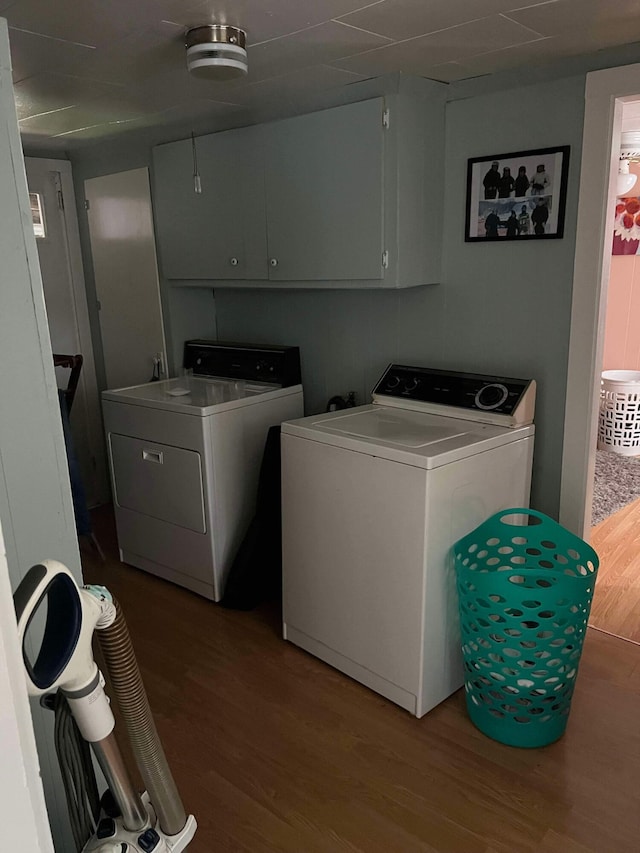 clothes washing area with washing machine and dryer, wood finished floors, and cabinet space