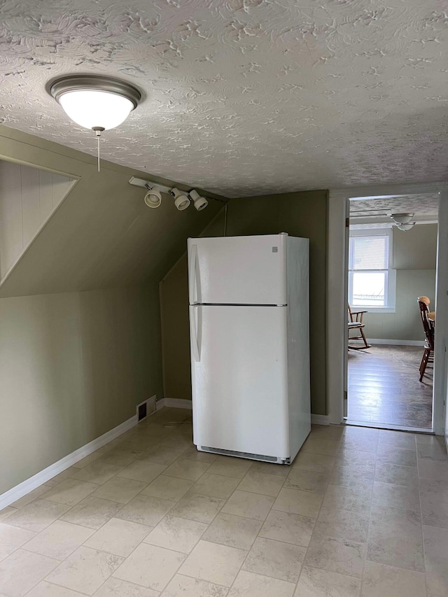 kitchen with white fridge, a textured ceiling, and vaulted ceiling