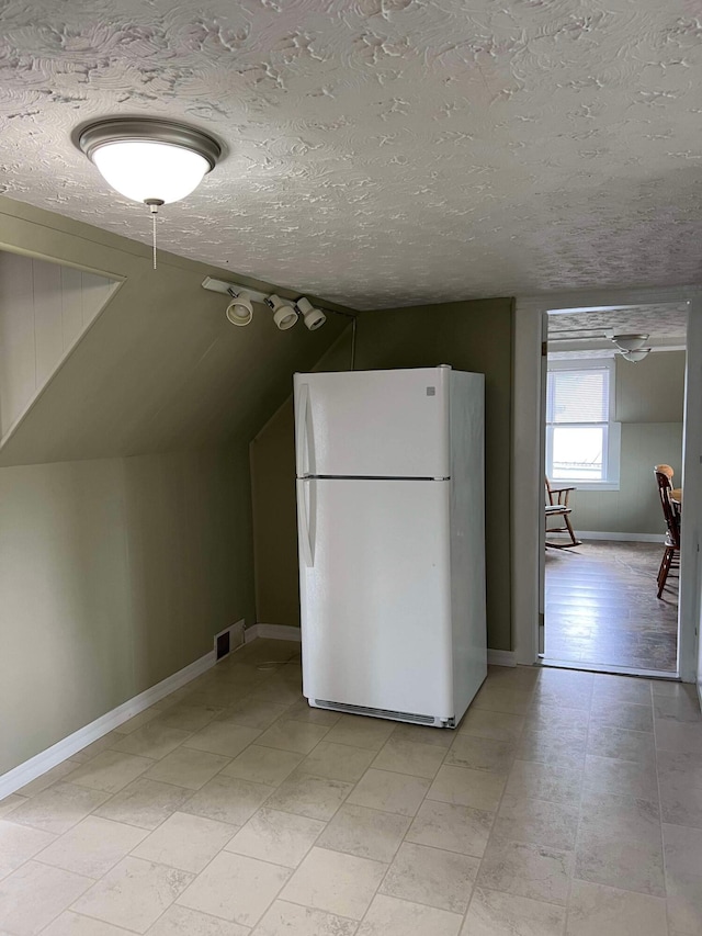 kitchen featuring freestanding refrigerator, a textured ceiling, lofted ceiling, baseboards, and visible vents