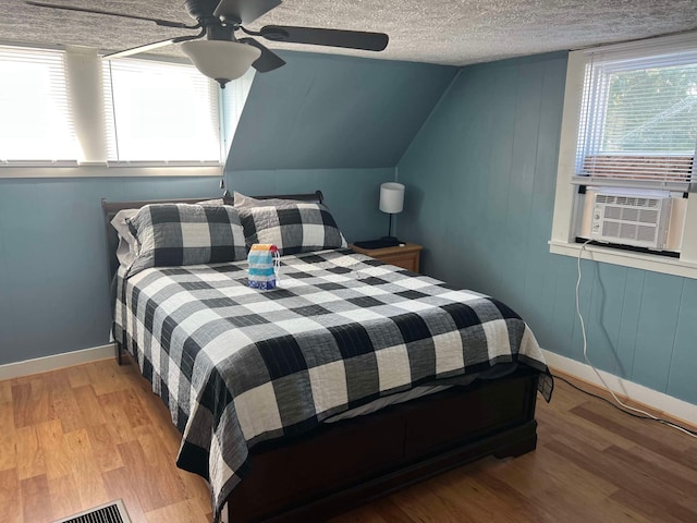 bedroom with ceiling fan, cooling unit, a textured ceiling, vaulted ceiling, and light wood-type flooring