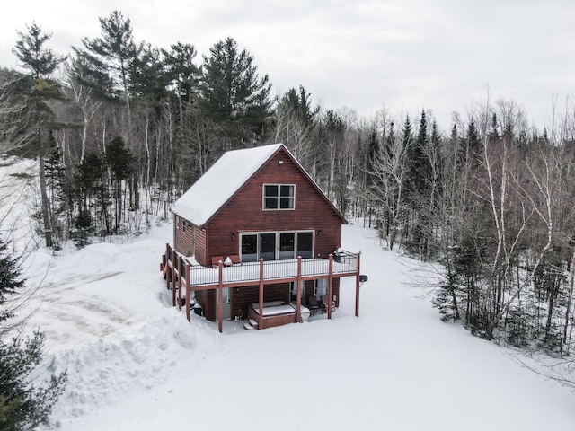 snow covered back of property featuring a wooded view and a wooden deck