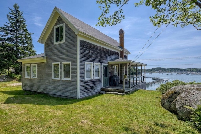 rear view of house featuring a water view and a lawn