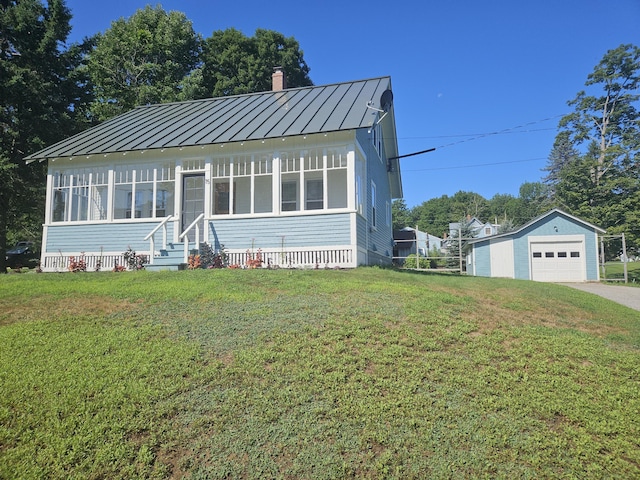 bungalow with a chimney, a standing seam roof, an outbuilding, a garage, and a front lawn