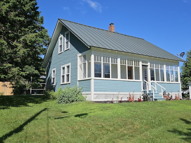 back of house with a chimney, a standing seam roof, a sunroom, and a lawn