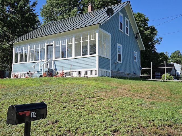 view of front of property with metal roof, a standing seam roof, a front yard, and a sunroom