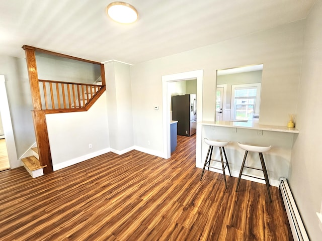 unfurnished living room featuring stairway, wood finished floors, a baseboard heating unit, and baseboards