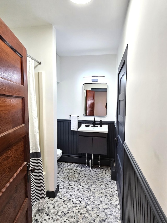 full bath featuring vanity, toilet, a shower with shower curtain, and wainscoting