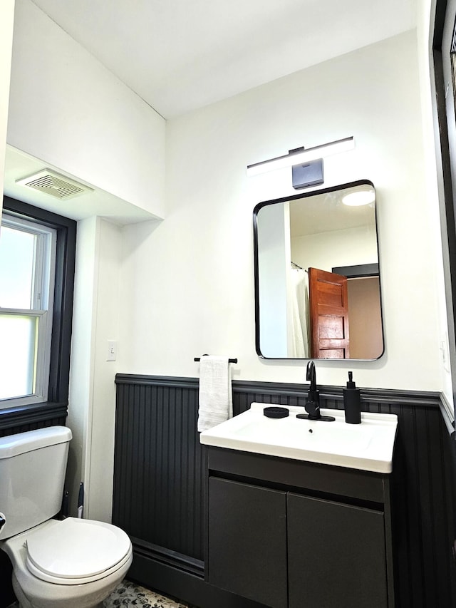 bathroom featuring visible vents, toilet, a wainscoted wall, and vanity