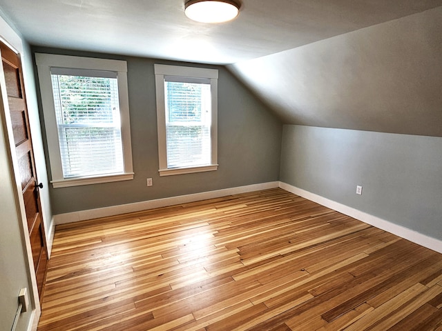 additional living space featuring a healthy amount of sunlight, light wood-style flooring, and vaulted ceiling