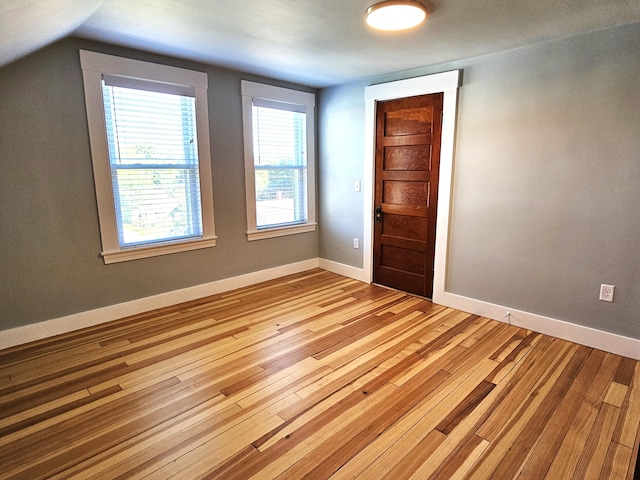 spare room featuring light wood finished floors, vaulted ceiling, and baseboards