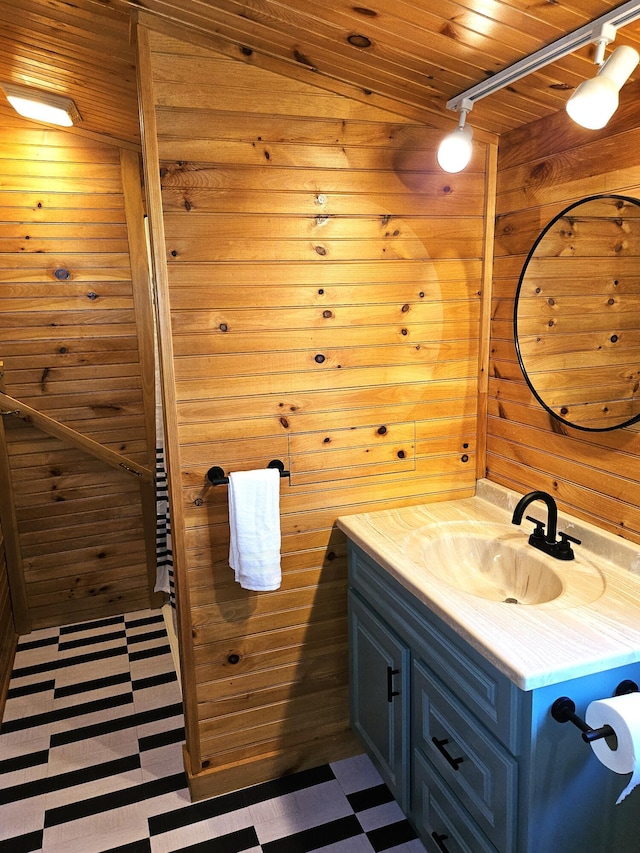 bathroom featuring tile patterned floors, wood walls, rail lighting, and vanity