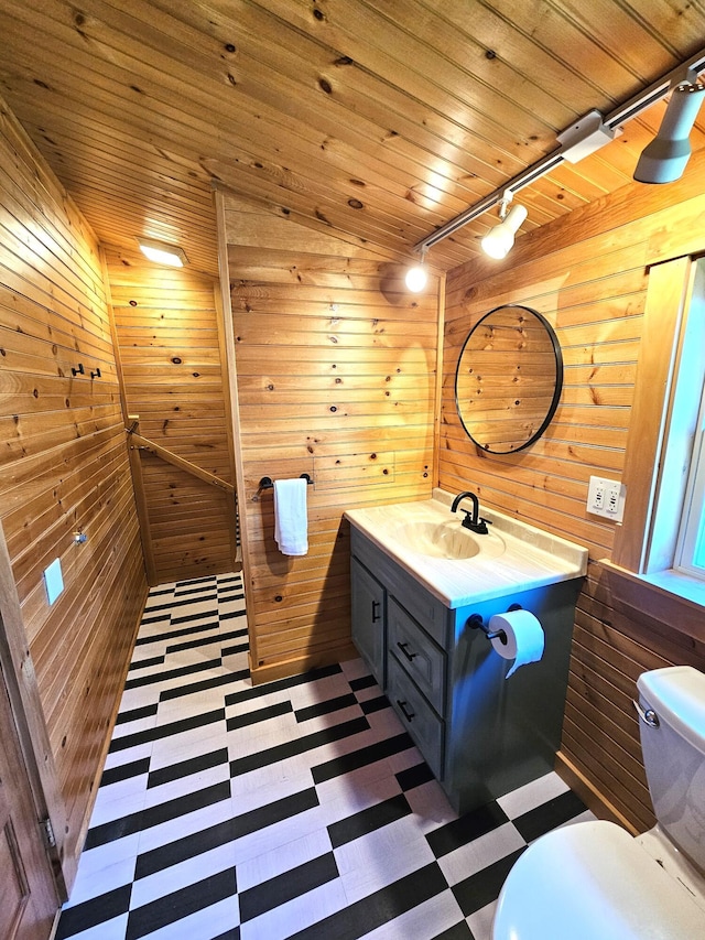 half bath with wood walls, toilet, tile patterned floors, and track lighting