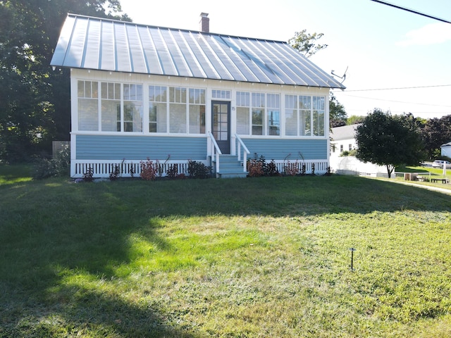 bungalow featuring a standing seam roof, a front lawn, metal roof, a chimney, and entry steps