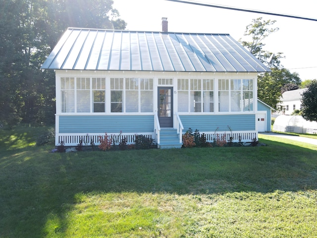 bungalow-style home with a standing seam roof, metal roof, a chimney, a front lawn, and a sunroom
