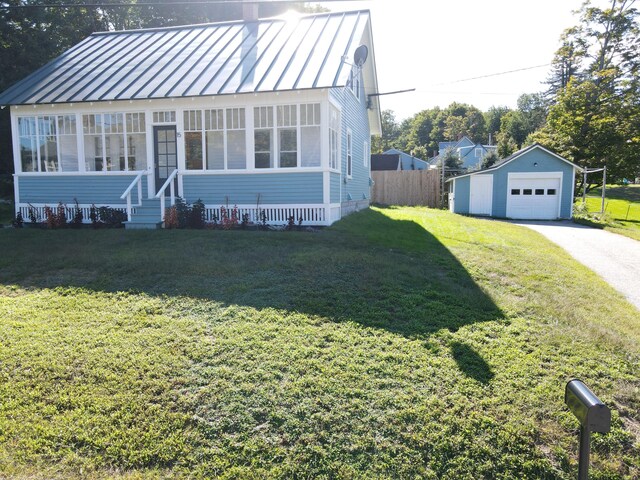 view of front of property featuring a standing seam roof, an outbuilding, driveway, a detached garage, and a front lawn