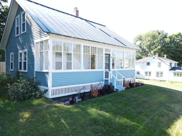 rear view of house with a chimney, a yard, a standing seam roof, metal roof, and a sunroom