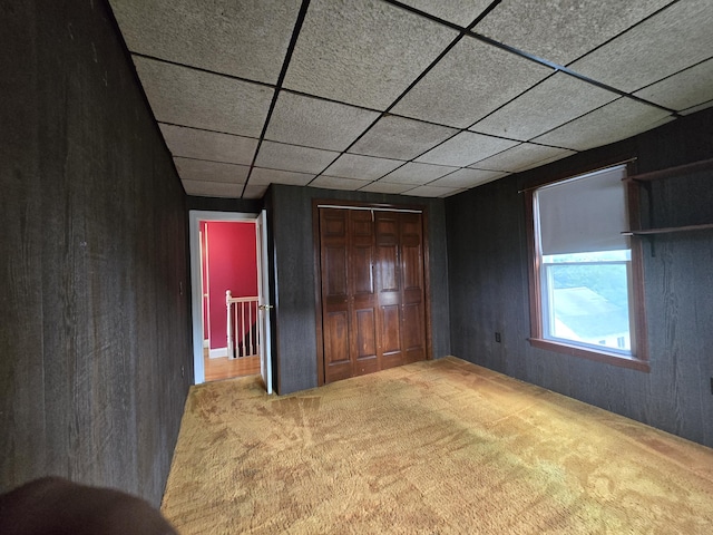 unfurnished bedroom featuring carpet, a closet, and wood walls