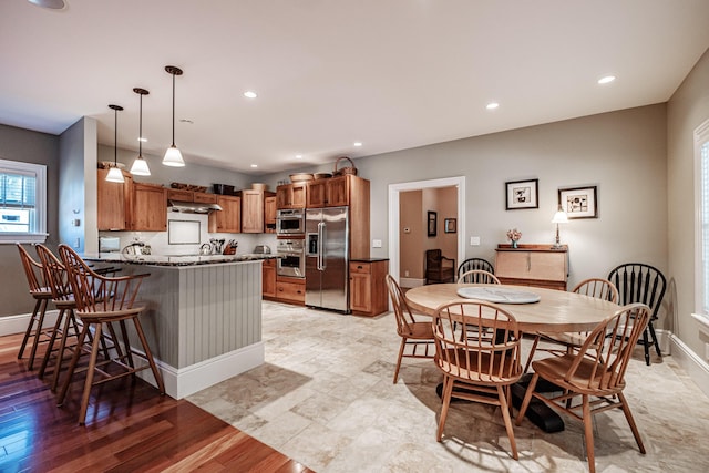 kitchen featuring appliances with stainless steel finishes, a breakfast bar, range hood, dark stone countertops, and hanging light fixtures