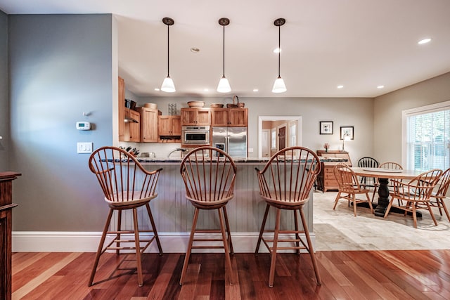 kitchen featuring hanging light fixtures, kitchen peninsula, light wood-type flooring, and stainless steel fridge with ice dispenser