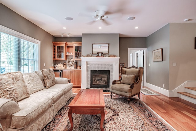 living room with ceiling fan, a tiled fireplace, and light hardwood / wood-style flooring