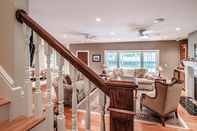 living room featuring a tiled fireplace, ceiling fan, and light hardwood / wood-style flooring