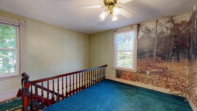 spare room featuring dark carpet, a textured ceiling, ceiling fan, and a healthy amount of sunlight