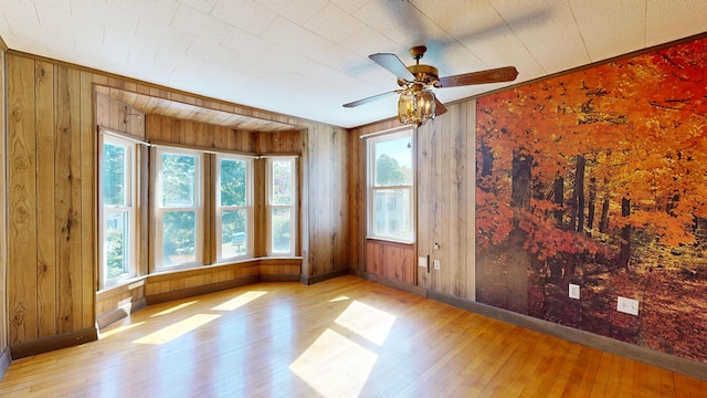 spare room with ceiling fan, wooden walls, light hardwood / wood-style flooring, and plenty of natural light