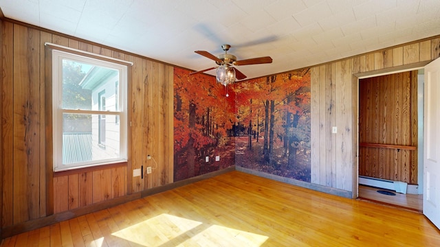 spare room featuring a baseboard heating unit, light wood-type flooring, wood walls, and ceiling fan