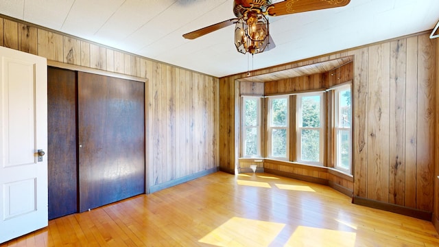 unfurnished bedroom with light hardwood / wood-style floors, wooden walls, ceiling fan, and a closet