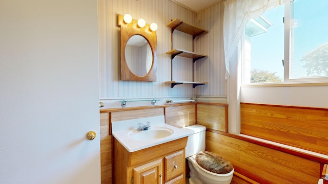 bathroom featuring vanity, wood walls, and toilet