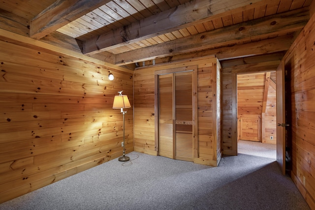 unfurnished bedroom with wooden walls, wood ceiling, beam ceiling, carpet flooring, and a closet