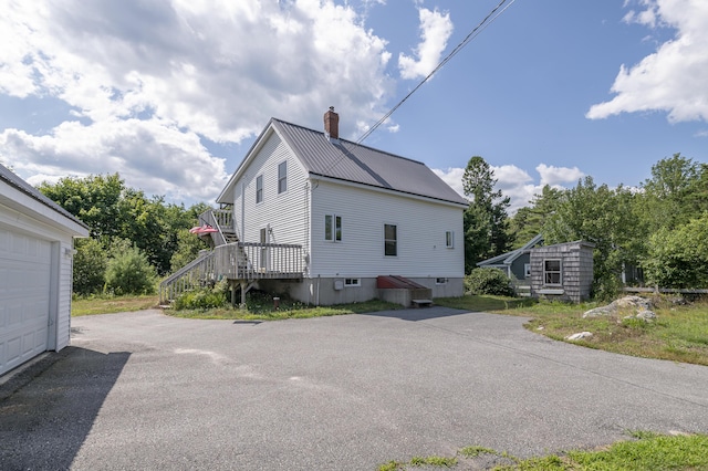 view of side of home with a garage, a chimney, metal roof, aphalt driveway, and an outbuilding