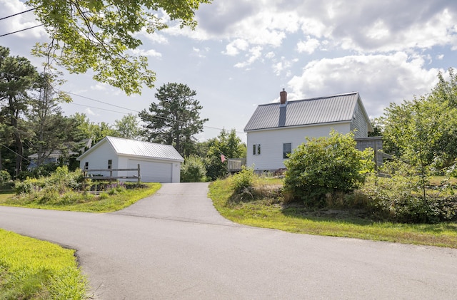 view of side of property with a detached garage, a chimney, metal roof, and an outdoor structure