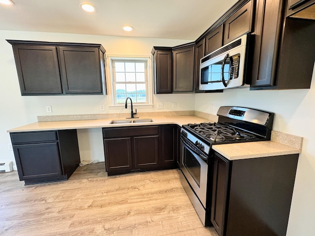 kitchen with light wood-style flooring, a sink, recessed lighting, appliances with stainless steel finishes, and dark brown cabinets