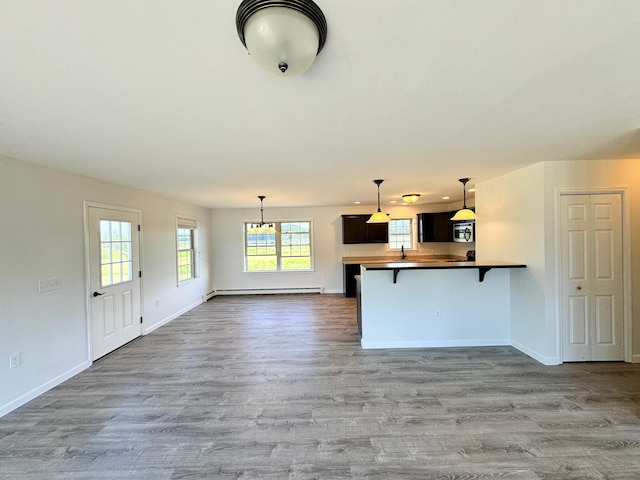 interior space with a breakfast bar area, wood finished floors, baseboards, a peninsula, and baseboard heating