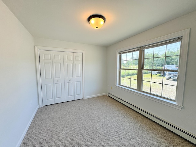 unfurnished bedroom featuring a closet, carpet flooring, a baseboard heating unit, and baseboards