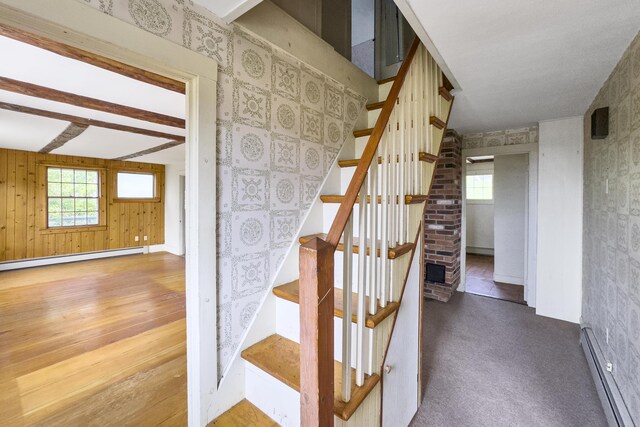 staircase featuring beam ceiling, carpet floors, a baseboard heating unit, and wooden walls