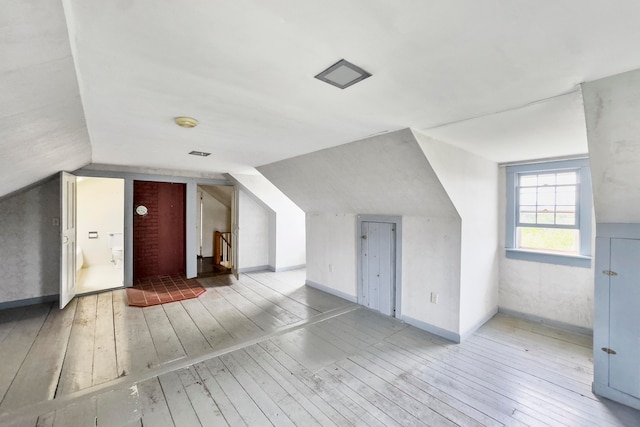 additional living space featuring lofted ceiling, hardwood / wood-style floors, and brick wall