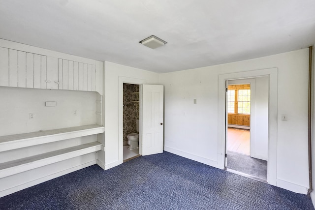 unfurnished bedroom with ensuite bath, baseboards, dark carpet, and a baseboard heating unit
