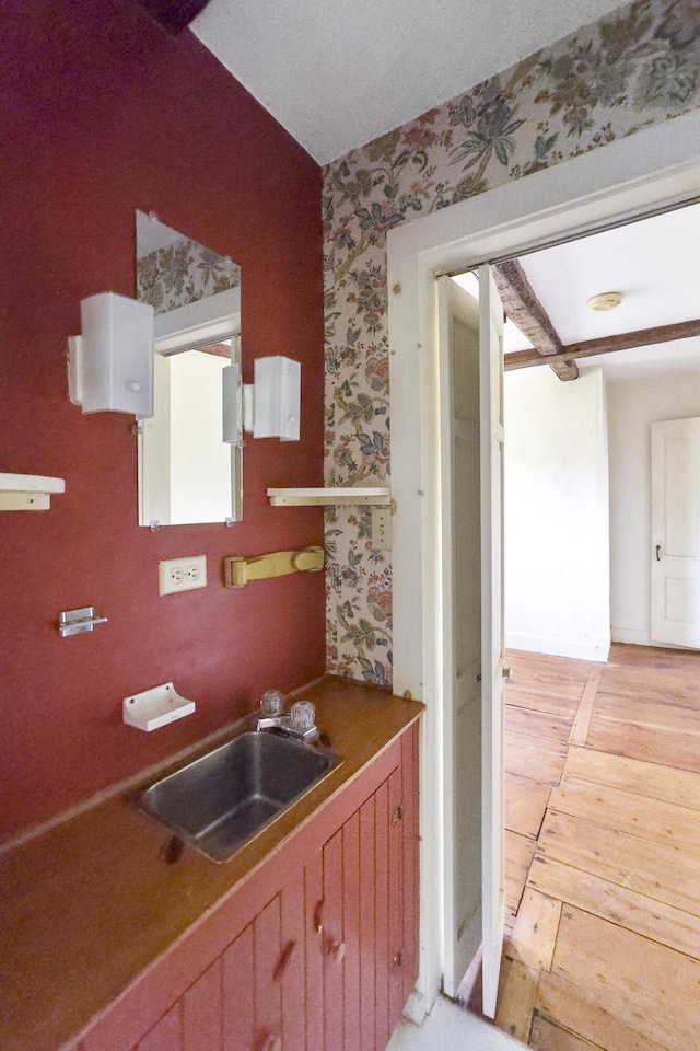 kitchen with wallpapered walls, a sink, and light wood finished floors